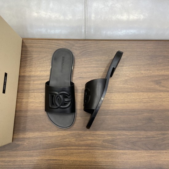 Top and angled view of black calfskin slides next to a branded box on a wooden surface in black and white