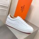 Hermes Boomerang White Leather Trainer Side Profile View Side profile view of the right Hermes Boomerang white leather low-top trainer with orange brand box in background.