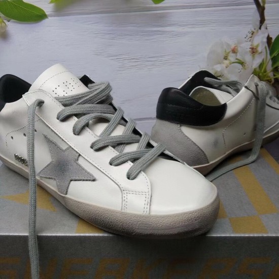 Golden Goose Super-Star Trainers - Shoebox Display in white and grey Front and side view of Golden Goose Super-Star white leather trainers resting on a shoebox in white and grey
