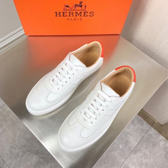Top-down view of both Hermès white leather low top trainers arranged on a metallic counter in white and orange