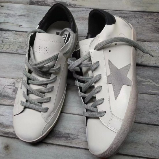 Golden Goose Super-Star White Trainers - Angled View in white and grey Pair of Golden Goose Super-Star white trainers displayed angled on a grey wood backdrop