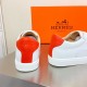 Rear view showing the orange leather heel tabs and embossed midsole branding on Hermès trainers in white and orange