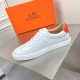 Full lateral side view of the Hermès white leather trainer with orange heel accent
