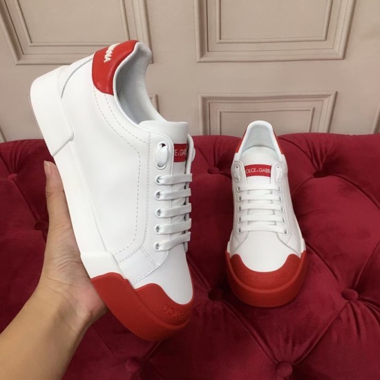 Hand holding a white trainer alongside its pair, showing tongue patch and red detailing