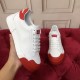 Hand holding a white trainer alongside its pair, showing tongue patch and red detailing