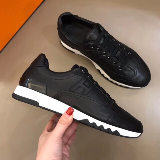 Hermes Trail low top black leather trainer held at side profile angle in black and white