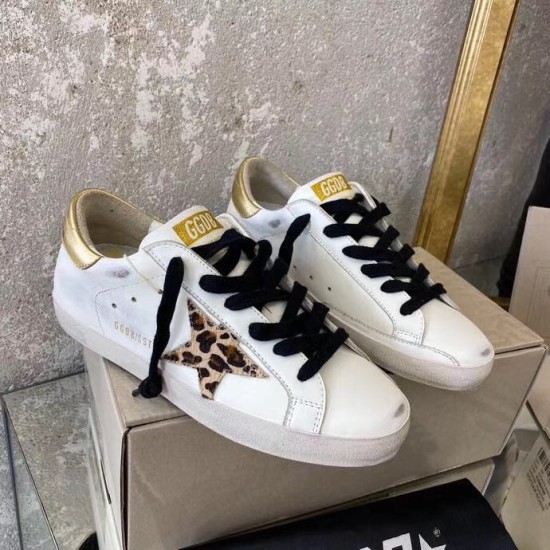 Golden Goose Super-Star Trainers Side Profile in white and gold Pair of Golden Goose white leather low-top trainers with black laces resting on shoebox