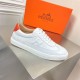 Single Hermès white leather low top trainer featuring orange heel trim on display