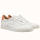 Pair of Hermès white leather low top trainers with orange heel tabs shown at a three-quarter angle