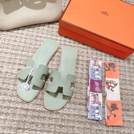 Hermes Oran Flat Sandals In Light Green - Flat Lay with Accessories Top view of light green sandals shown next to two patterned silk twill ribbons and a box