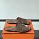 Hermes Izmir Sandals In Beige angled pair resting on an orange box