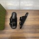 Angled top view of black Gucci slide sandals with branded insoles beside a green box in black and silver
