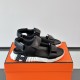 Hermes black leather junior sandals resting on an orange box side angle in black and white
