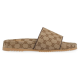 Side profile view of the beige and brown canvas slide sandal showing the flat sole and wide strap