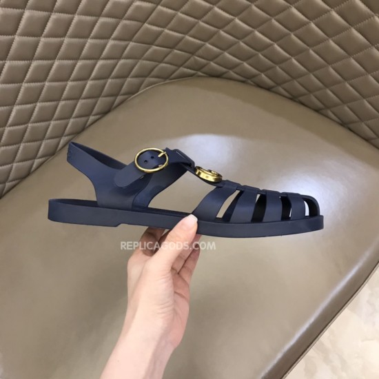 Gucci Blue Rubber Sandals Held Side Profile in blue and white Gucci rubber buckle strap sandals in blue held up against a quilted brown background showing the heel strap and buckle in blue and white