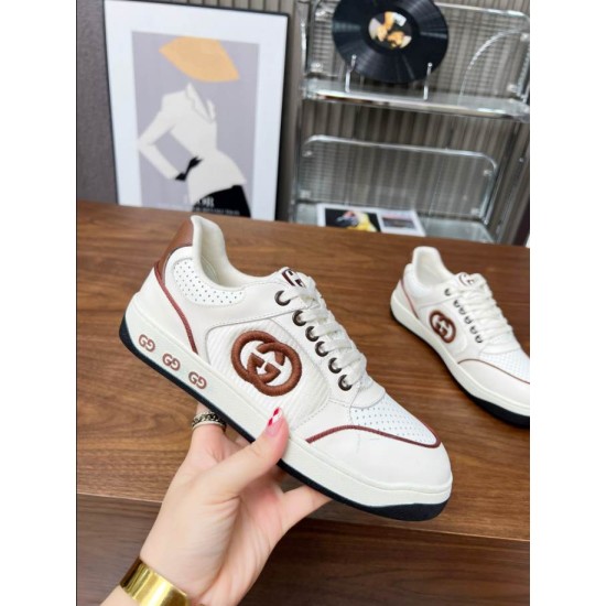 Hand holding Gucci white trainer highlighting side logo patch and sole branding in white and brown