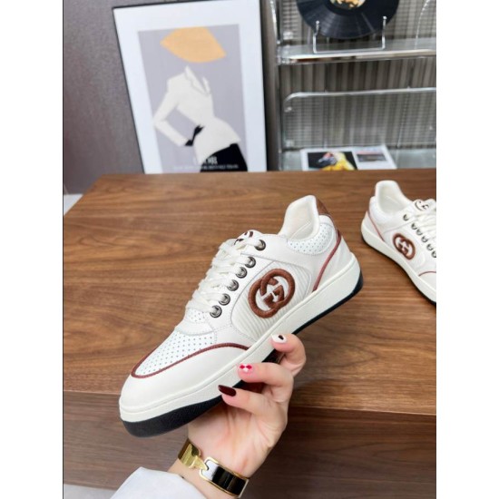 Hand holding Gucci white leather trainer showing side logo and sole in white and brown