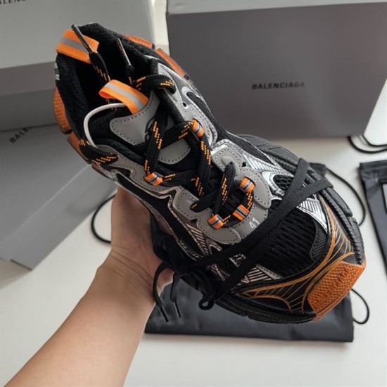 Handheld top view displaying the collar, heel pull tab, and tongue of the Balenciaga trainer in black and orange