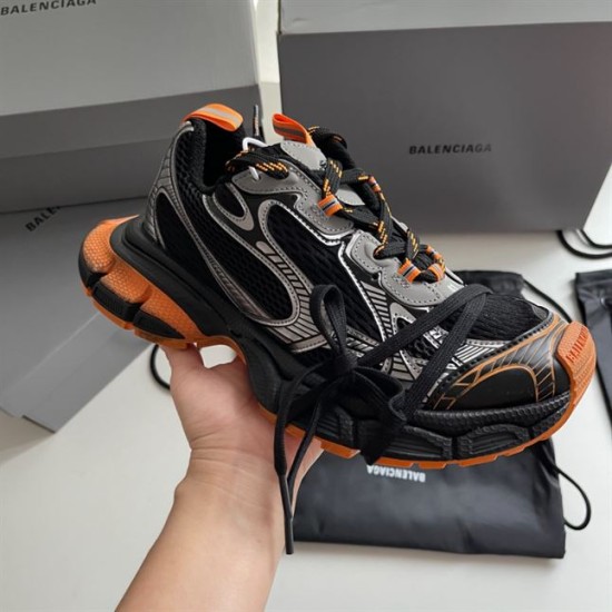 Handheld view showcasing the side panel construction of the black and orange Balenciaga trainer