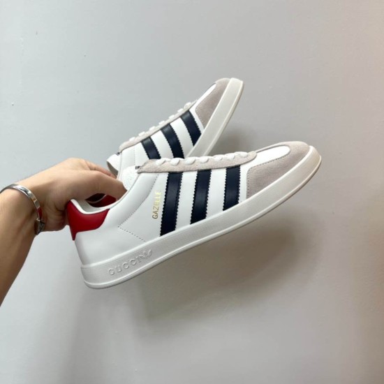 Handheld View of Gucci Gazelle White Trainer in white and black Hand holding Gucci Gazelle white leather trainer showcasing the lateral side design in white and black