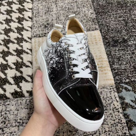 Angled front view of Christian Louboutin trainer held in hand showing black patent toe in black and white