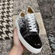 Angled front view of Christian Louboutin trainer held in hand showing black patent toe in black and white