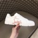 Lateral side view of Christian Louboutin white trainer held in hand showing red signature details