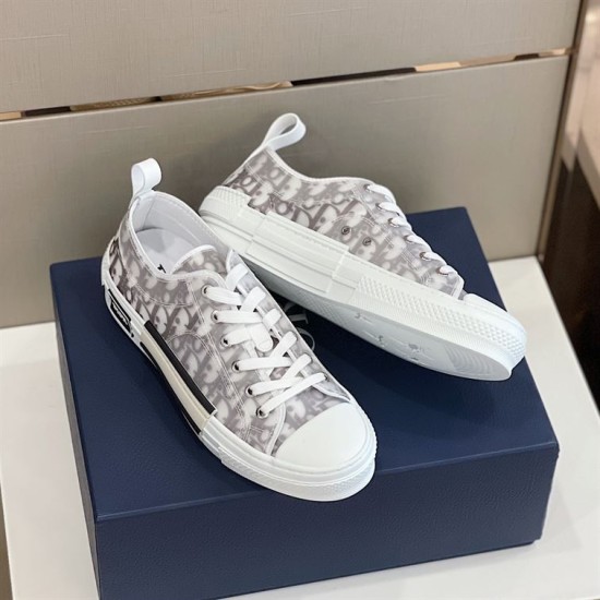 Angled view of a pair of grey and white Dior B23 trainers resting on box