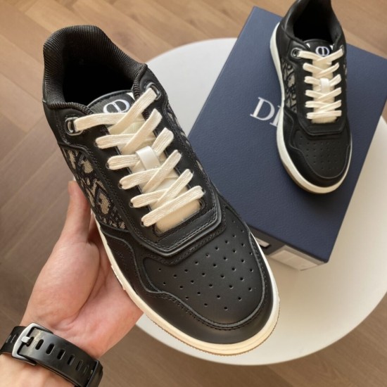 Hand holding black Dior B27 trainer highlighting upper eyelets and perforated toe in black and white