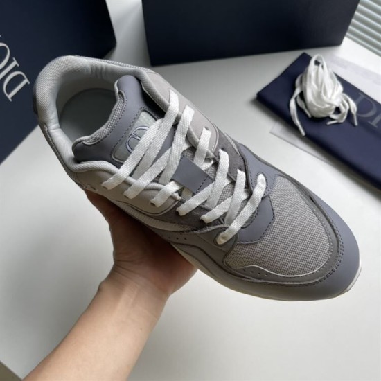 Hand holding a single Dior B29 grey trainer highlighting upper mesh texture and lacing in grey and white