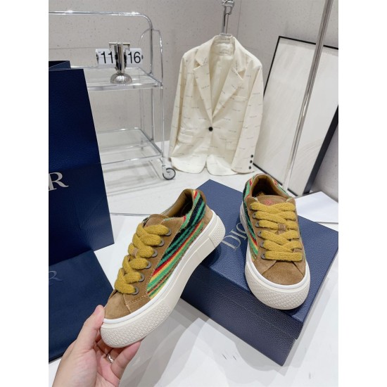 Dior B33 Trainer Handheld View in brown and yellow Hand holding a Dior B33 brown suede trainer showing cream sole and striped panel in brown and yellow