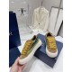 Dior B33 Trainer Handheld View in brown and yellow Hand holding a Dior B33 brown suede trainer showing cream sole and striped panel in brown and yellow