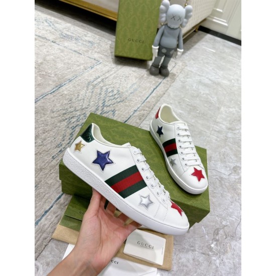 Hand holding single Gucci Ace Embroidered white leather trainer showing side web stripe and metallic star patches in white and green