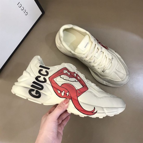 Gucci Rhyton Trainer Handheld Lateral View in off white Off white Gucci Rhyton trainer held in hand showing side graphic print