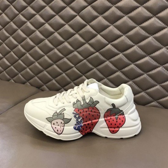 Gucci Rhyton Strawberry Print Side View in ivory and red Gucci Rhyton ivory trainer placed on leather surface highlighting outer print in ivory and red