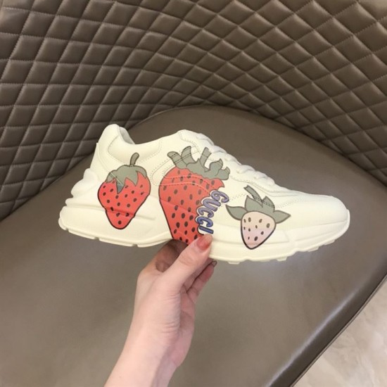Gucci Rhyton Strawberry Graphic Detail View in ivory and red Hand holding single Gucci Rhyton ivory trainer showing lateral strawberry print in ivory and red