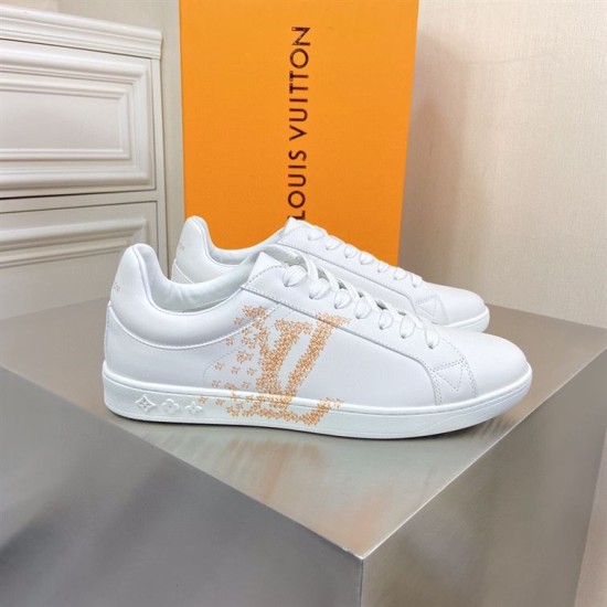 L classic white leather trainers with gold motif accent on display table L classic white leather trainers with gold motif accent displayed on a metallic surface