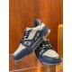 Front three-quarter view of L Trainer grey and navy blue leather sneakers resting on display stand