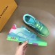 L Trainer Low Top Sneakers In Green Grained Leather - Overhead Angle in green and pink Top angle view of L trainer low top sneakers in green grained leather held against a quilted background in green and pink