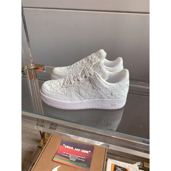 Angle View of L Air Force Embossed Monogram White Trainers Angled pair of L Air Force Embossed Monogram White Trainers on glass shelf