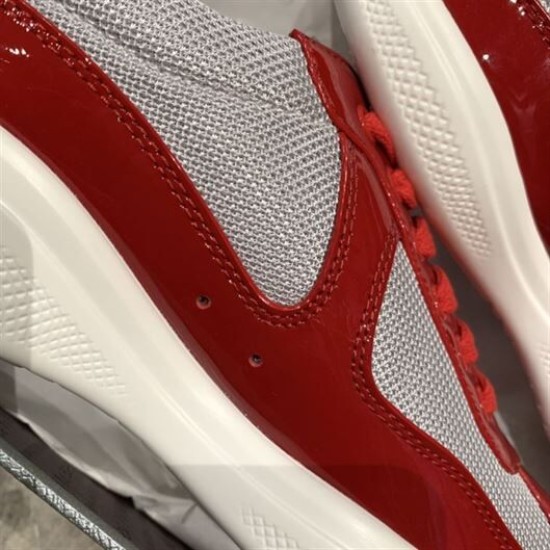 Close-up of red patent leather panels, grey mesh weave and side ventilation eyelets
