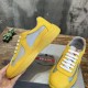 Prada yellow trainer held showing lateral side mesh panels and rubber sole in yellow and grey