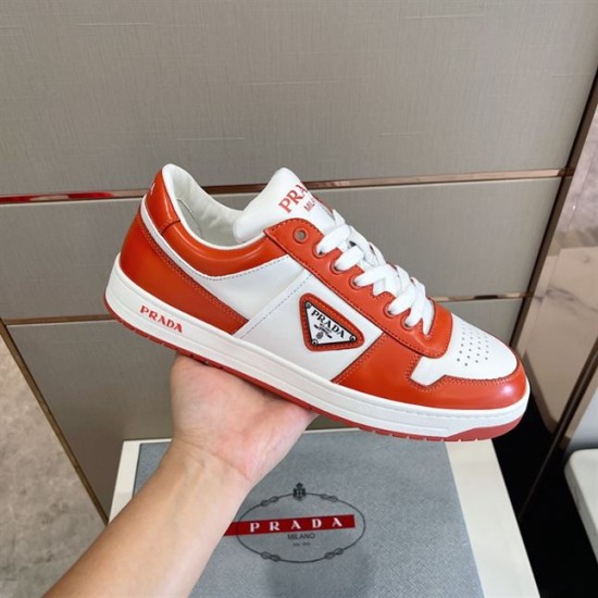 Handheld Side View of Prada Downtown Trainer in orange and white Hand holding single Prada Downtown leather trainer in orange and white showcasing lateral side detail