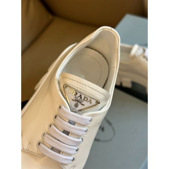 Prada Monolith Triangle Logo Badge Close-Up in white Close-up of metallic enamel logo badge on white leather tongue of Prada shoe