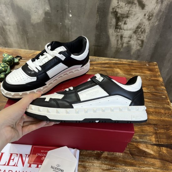 Lateral view of a Valentino Freedots black and white trainer held above its red luxury shoebox.